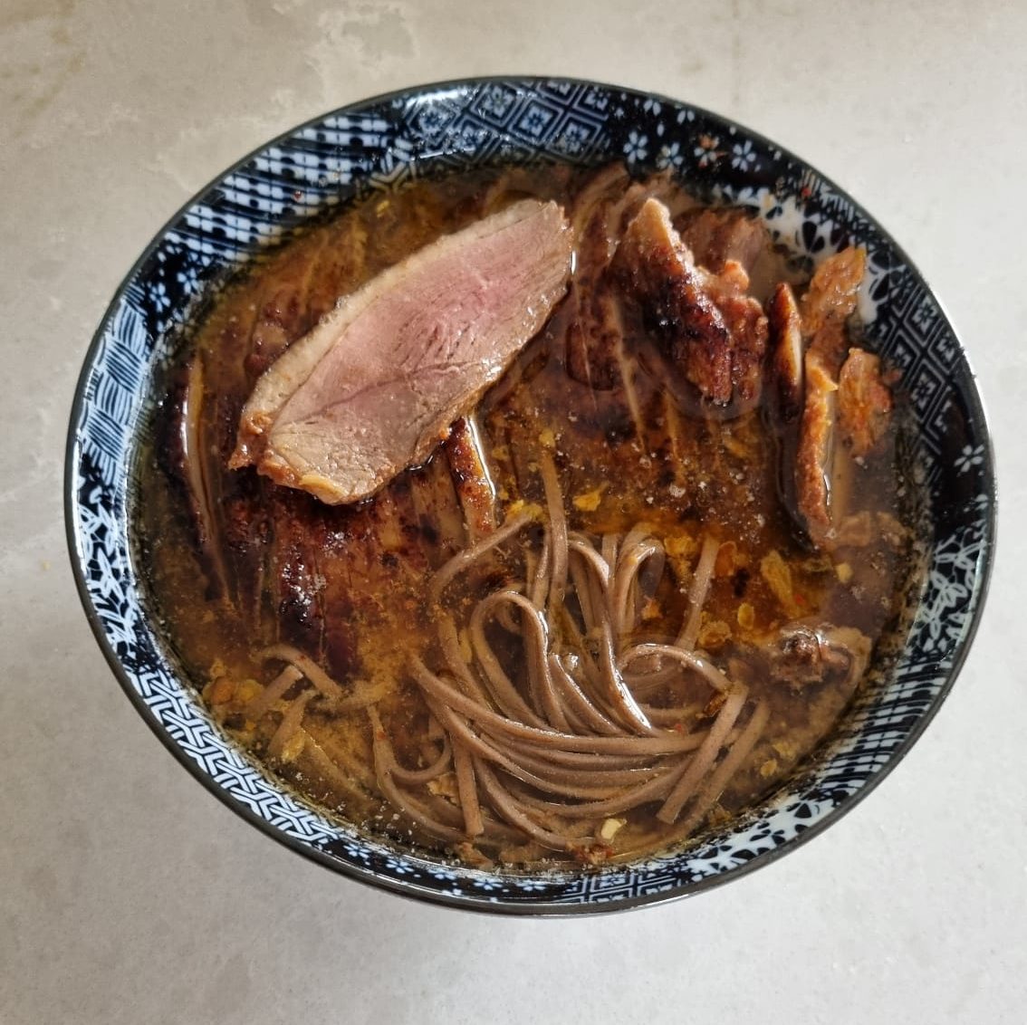 A vibrant bowl of leftover duck noodles with golden slices of crispy duck on top of miso broth and soba noodles, garnished with fresh scallions and a soft-boiled egg.