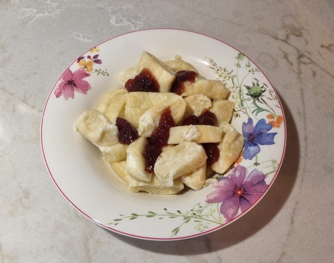 A plate of homemade lenivye vareniki, soft cheese dumplings made with tvorog, served with a spoonful of fruit jam and a drizzle of melted butter.