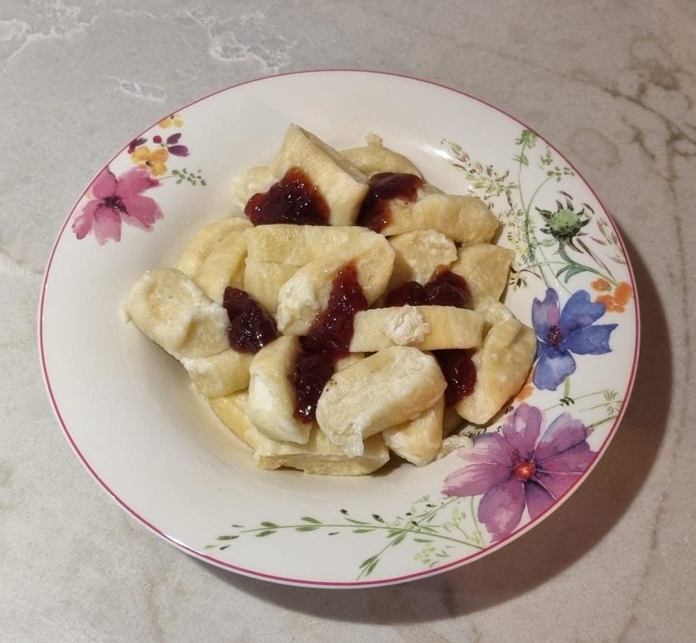A plate of homemade lenivye vareniki, soft cheese dumplings made with tvorog, served with a spoonful of fruit jam and a drizzle of melted butter.