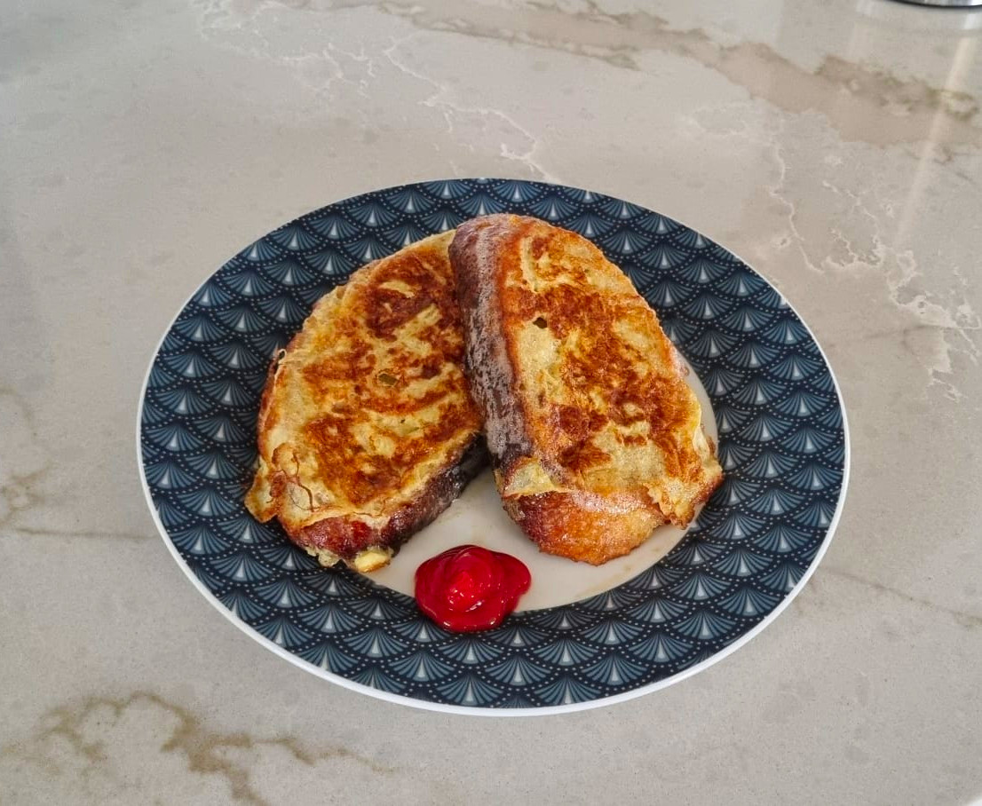 Two slices of savory French toast on a blue geometric patterned plate, with a dollop of red ketchup, on a marble countertop.