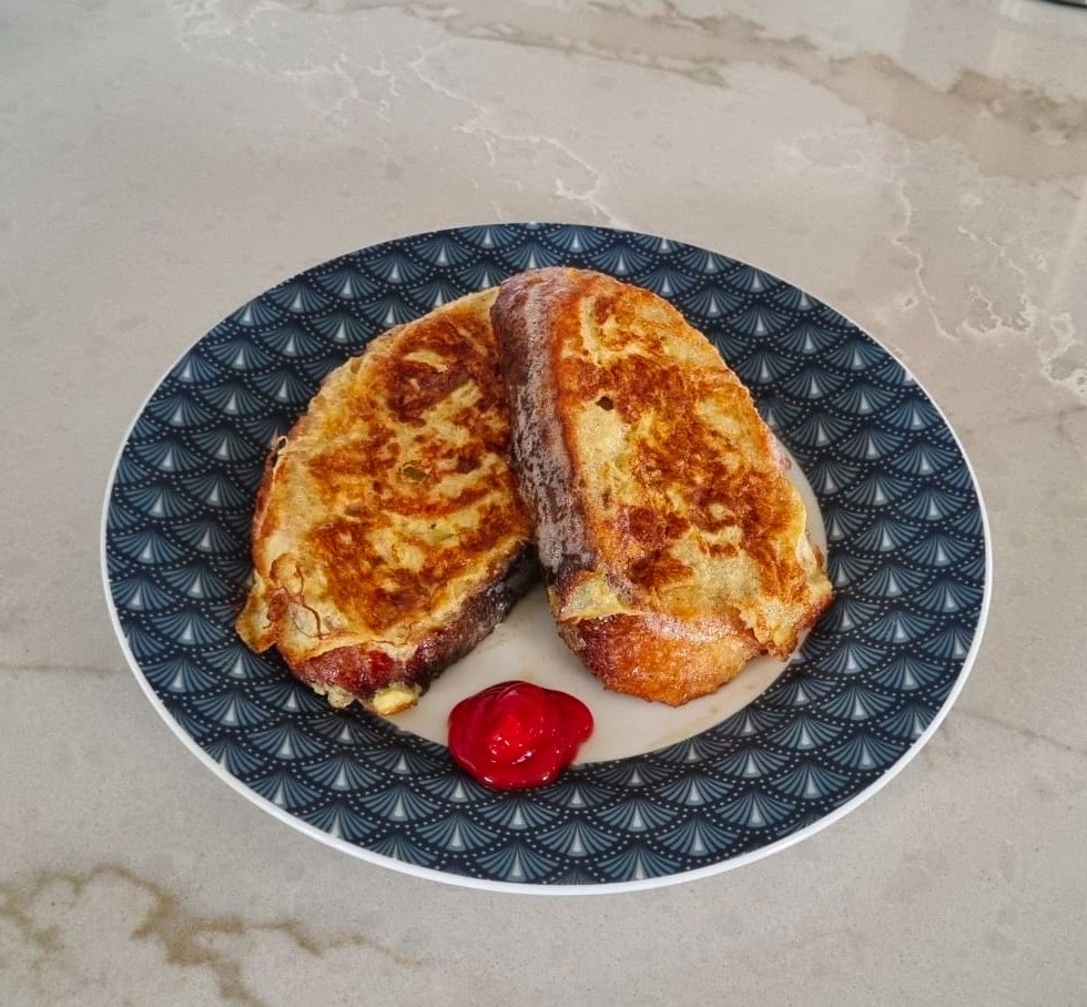 Two slices of savory French toast on a blue geometric patterned plate, with a dollop of red ketchup, on a marble countertop.