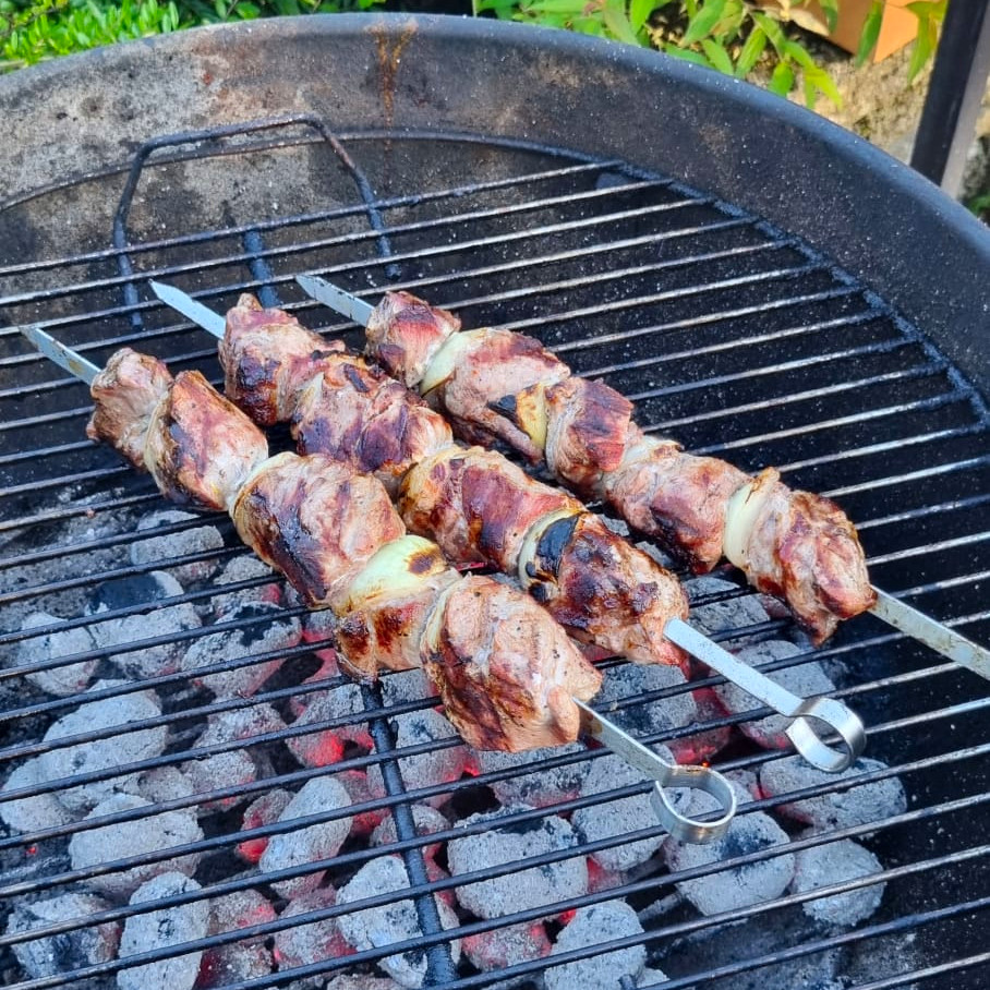 Three skewers of pork shashlyk and onions grilling over charcoal.